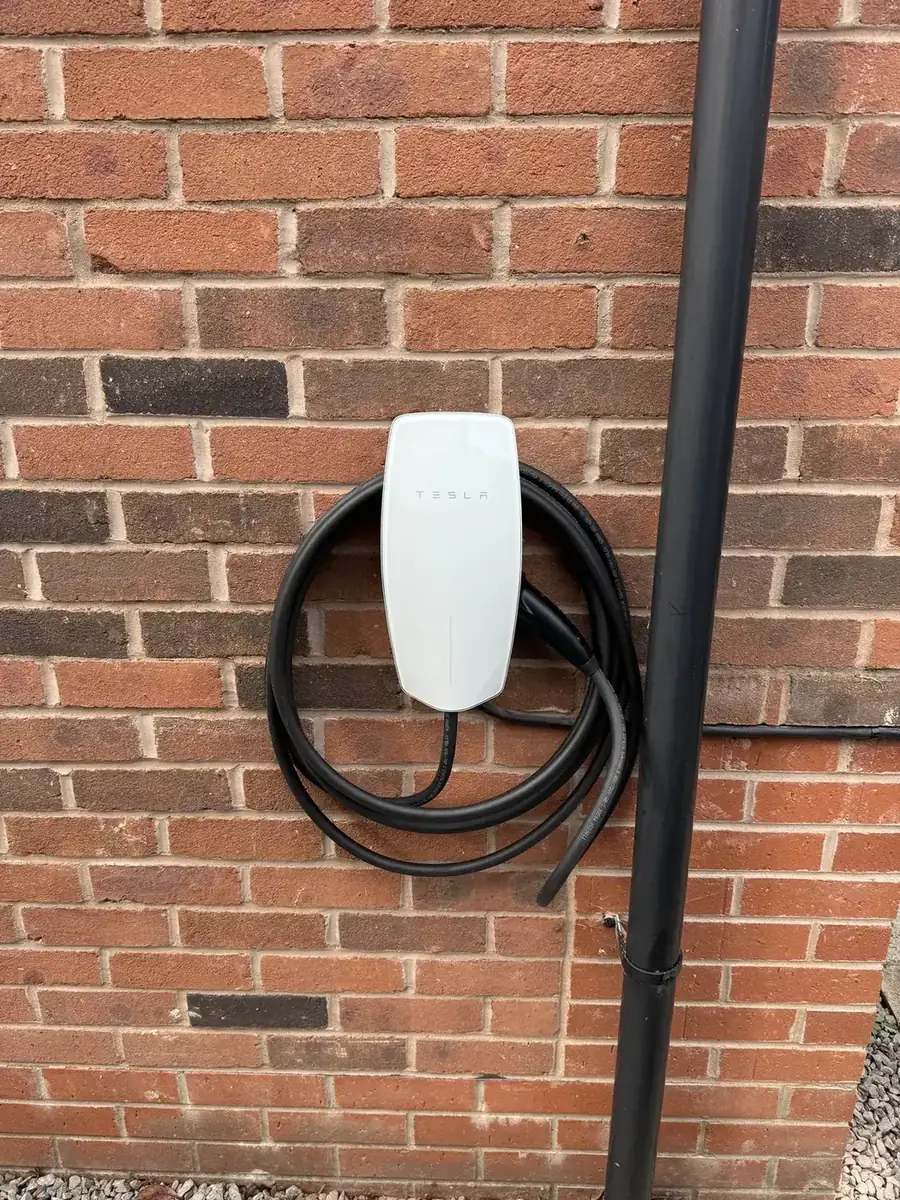 White EV charger with coiled cable fitted to a red brick wall