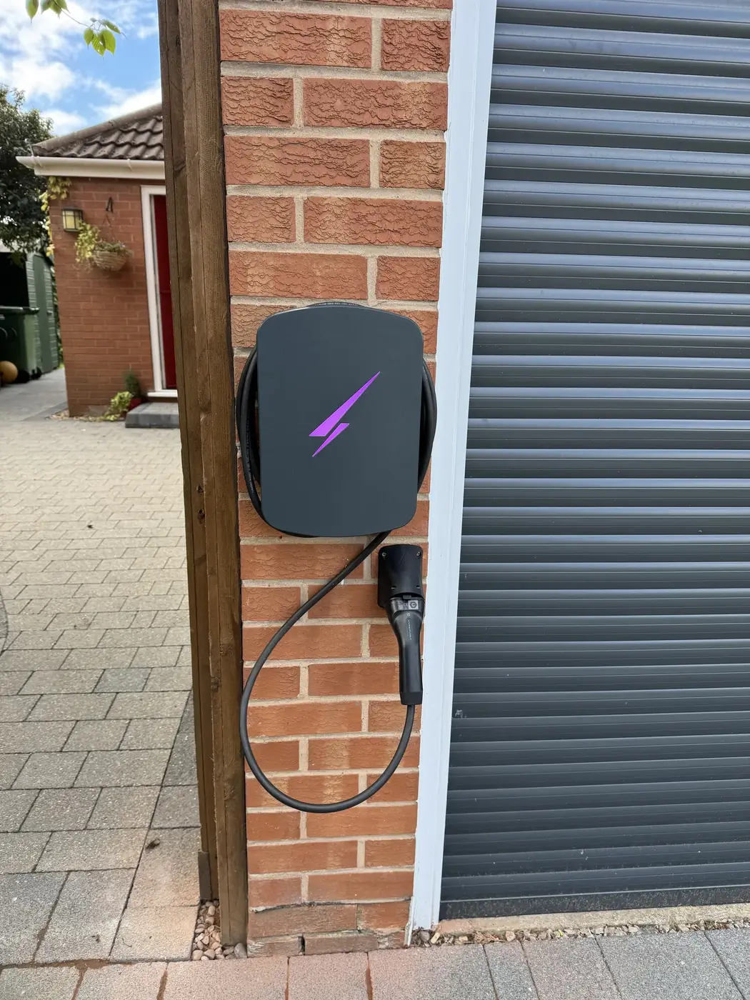 Dark grey EV charger fitted beside a garage door on a brick house